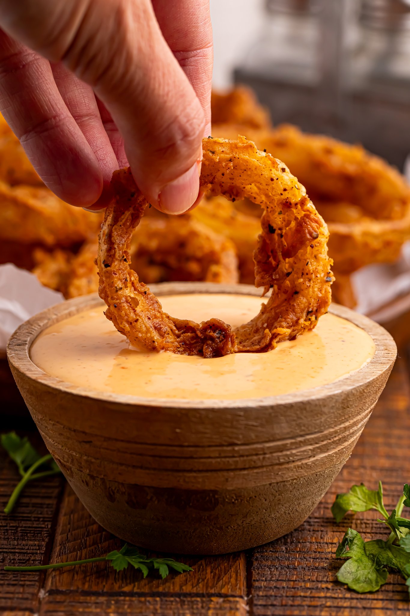 a Hand dipping a onion ring in sauce 