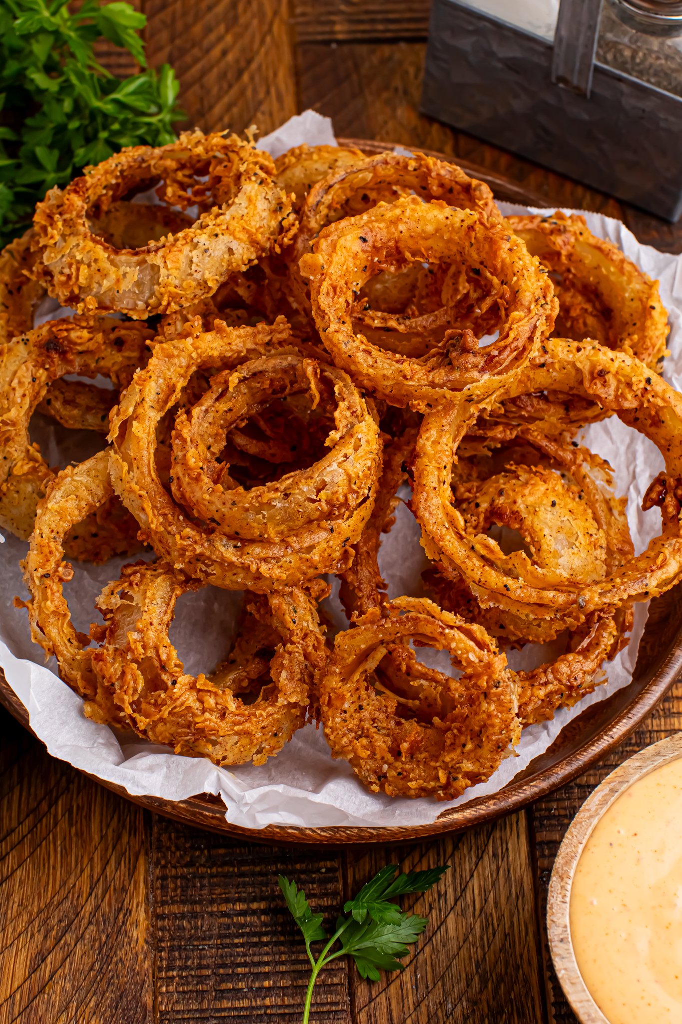 Homemade Deep Fried Onion Rings piled into a plate on table with a dipping sauce in a bowl in front