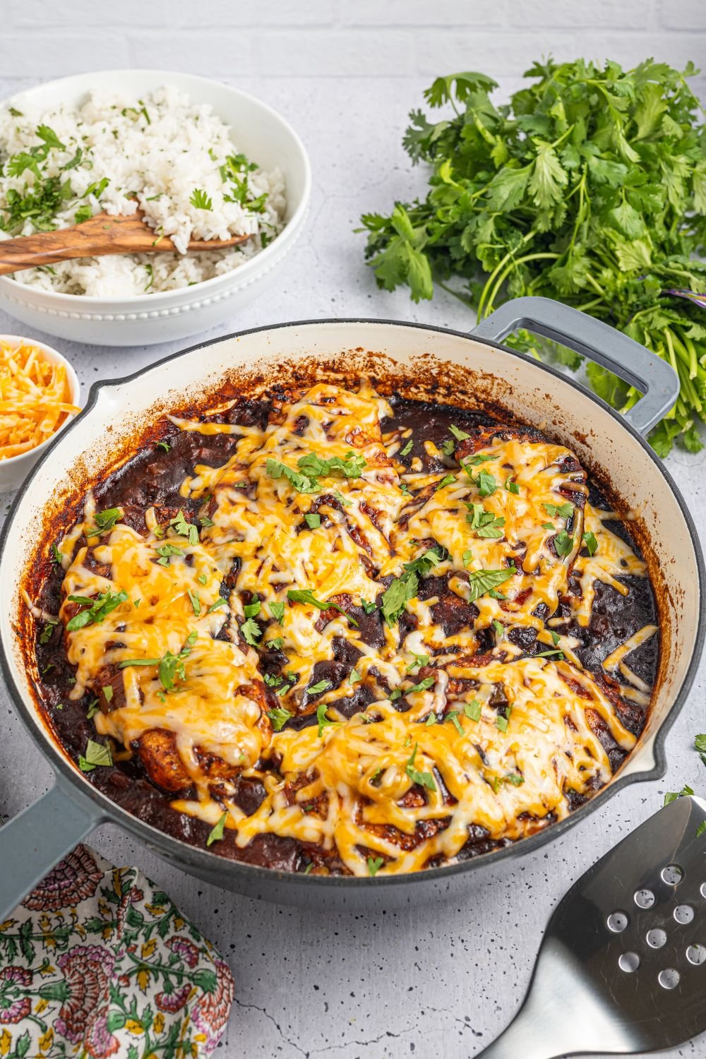 Cheesy Salsa Chicken in a skillet on table with parsley and rice and cheese in bowls 