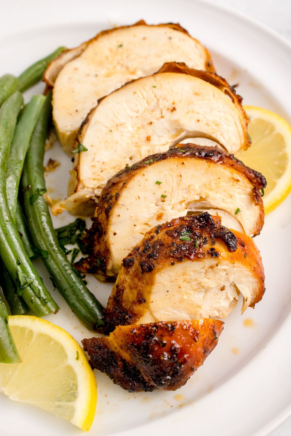 sliced Air Fryer Chicken Breast into strips on plate with green beans and lemon wedges to the side 