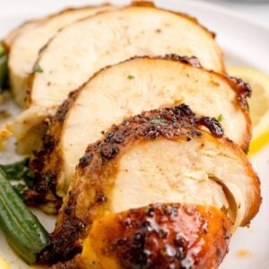 Air Fryer Chicken Breast sliced on table with some vegetables to side of the chicken