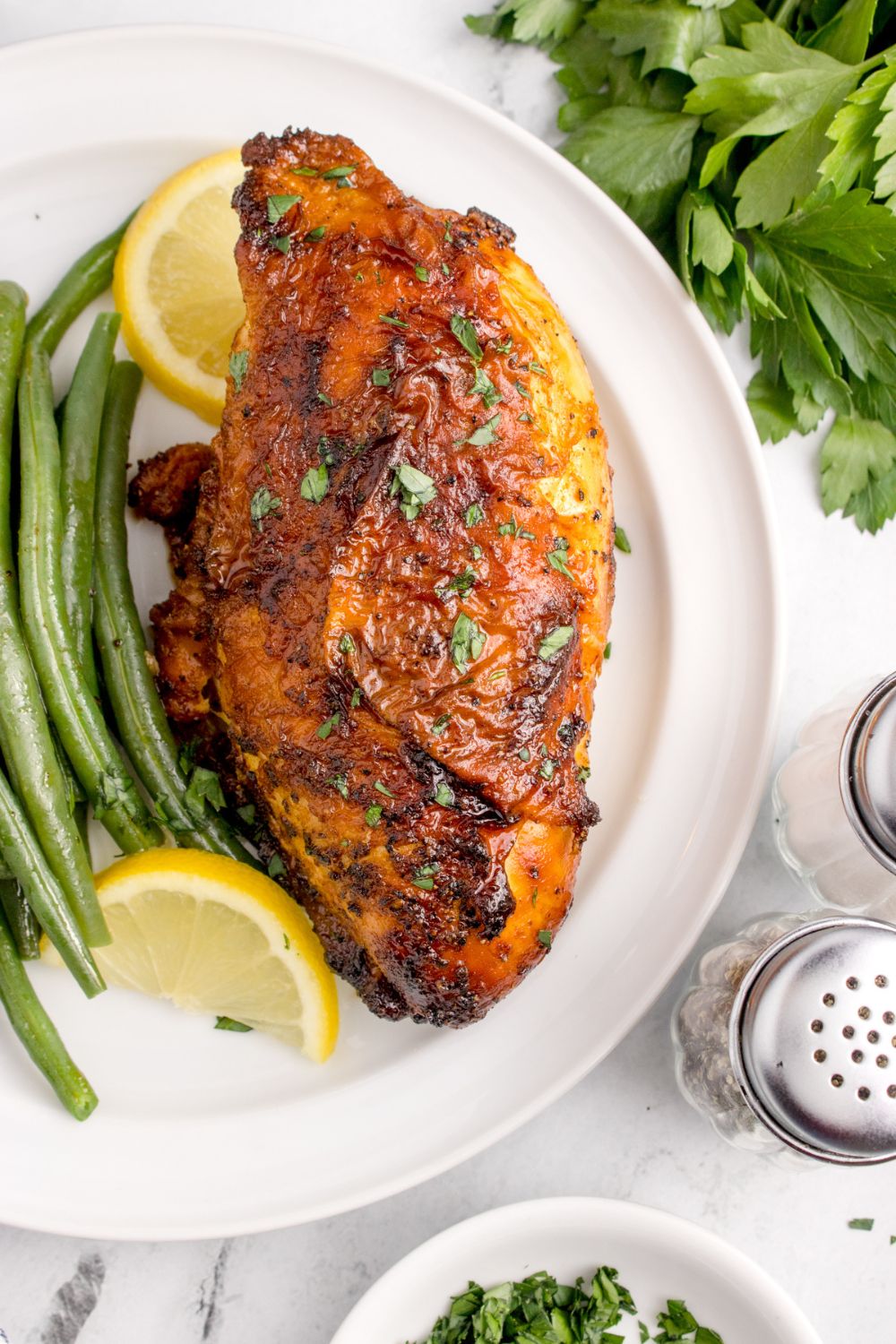 overhead look at table with Air Fryer Chicken Breast on plate withs some green beans, parsley, and salt and pepper to the side 