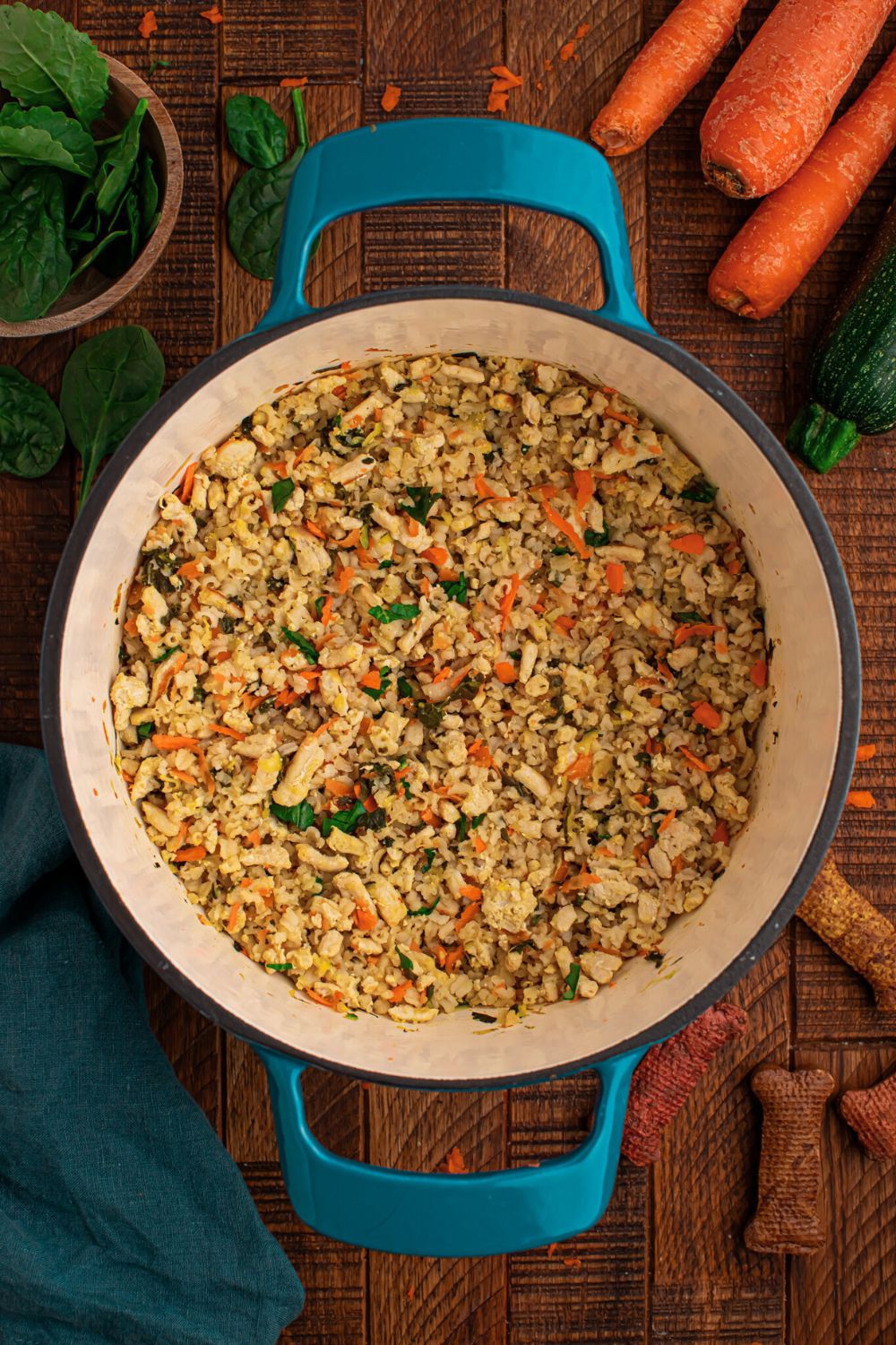 overhead look of Homemade Turkey and Rice Dog Food with Veggies in a blue pot with fresh herbs and whole carrots behind the pot on table 