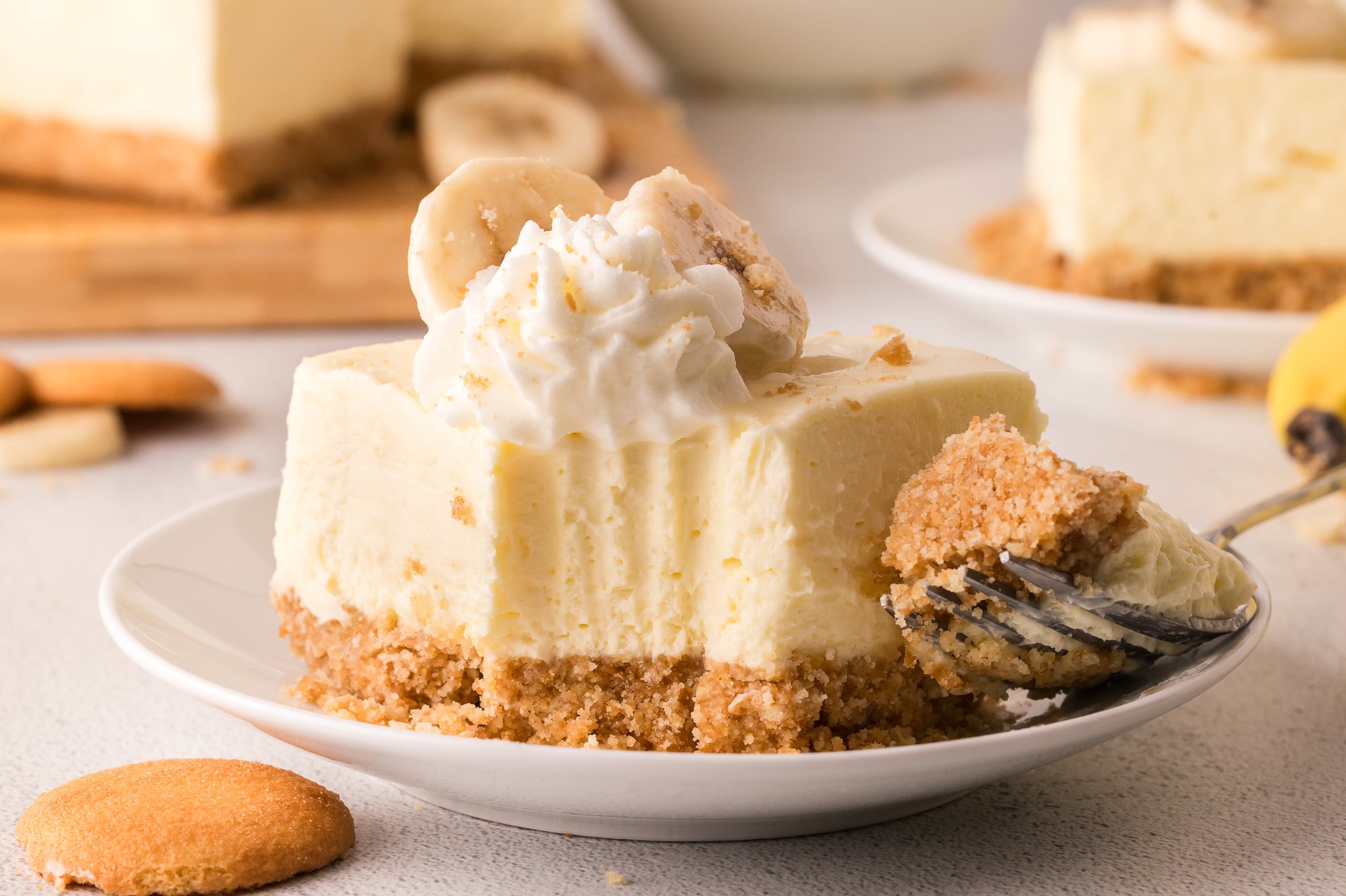 No Bake Banana Pudding Cheesecake Bar on a white plate with a fork bite taken out of it 