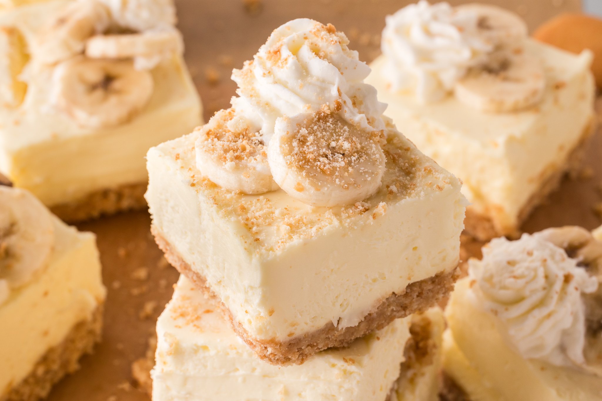 No Bake Banana Pudding Cheesecake Bars stacked on top of one another topped with crumbled vanilla wafers
