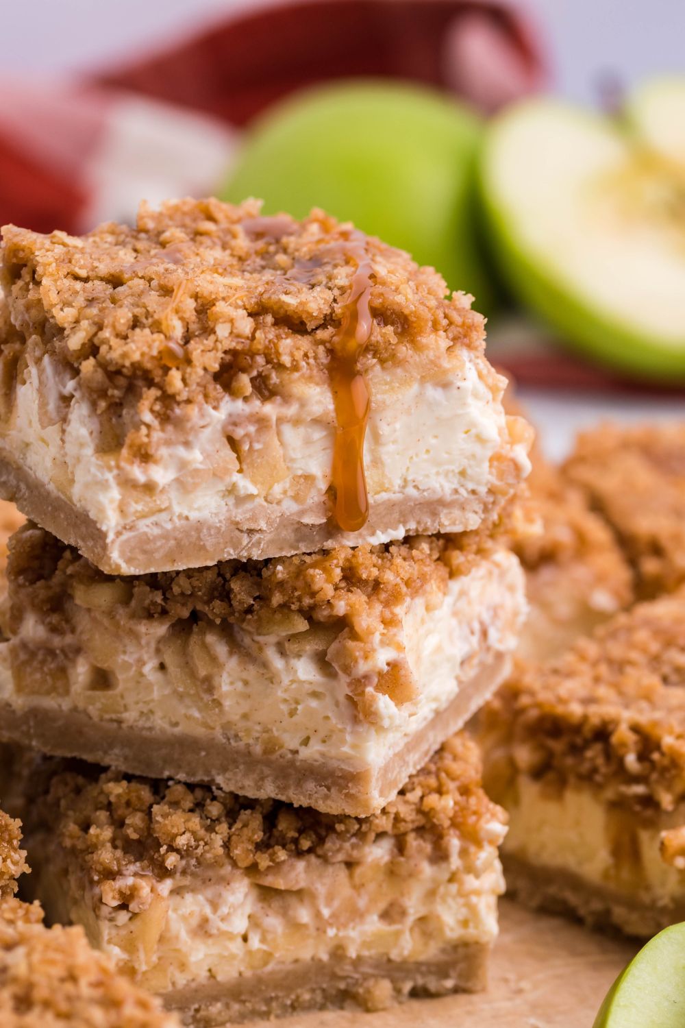 Caramel Apple Cheesecake Bars stacked on top of one another on table with apple sliced in half to side 