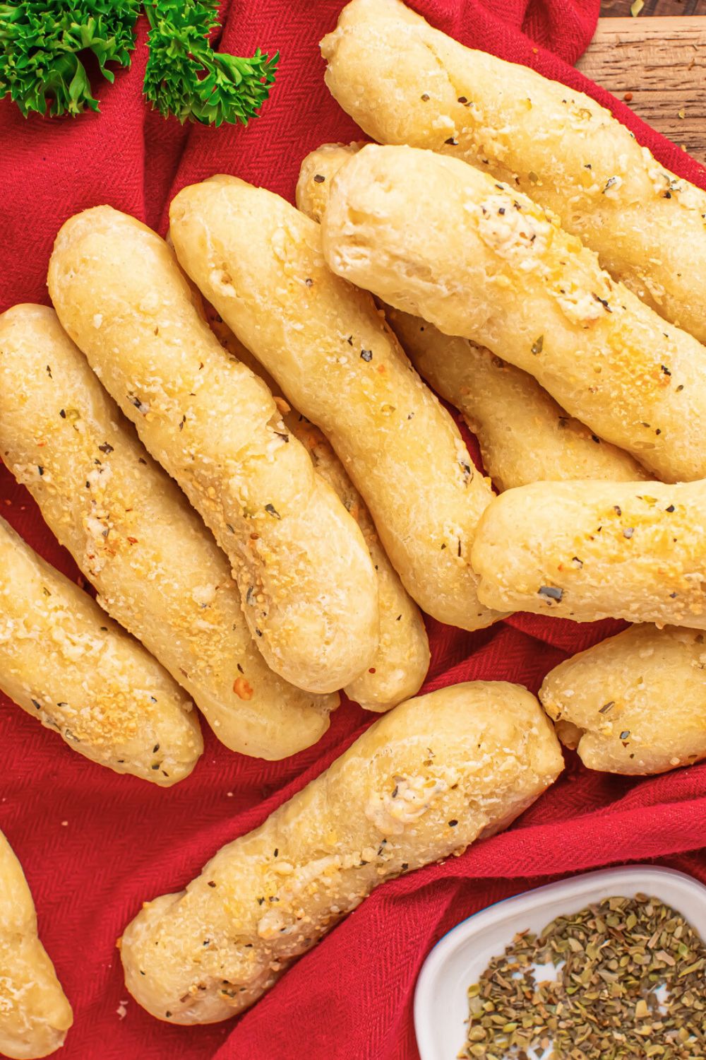 red towel with a stack of 2 Ingredient Garlic Parmesan Breadsticks on top and a bit of parsley behind it on table 