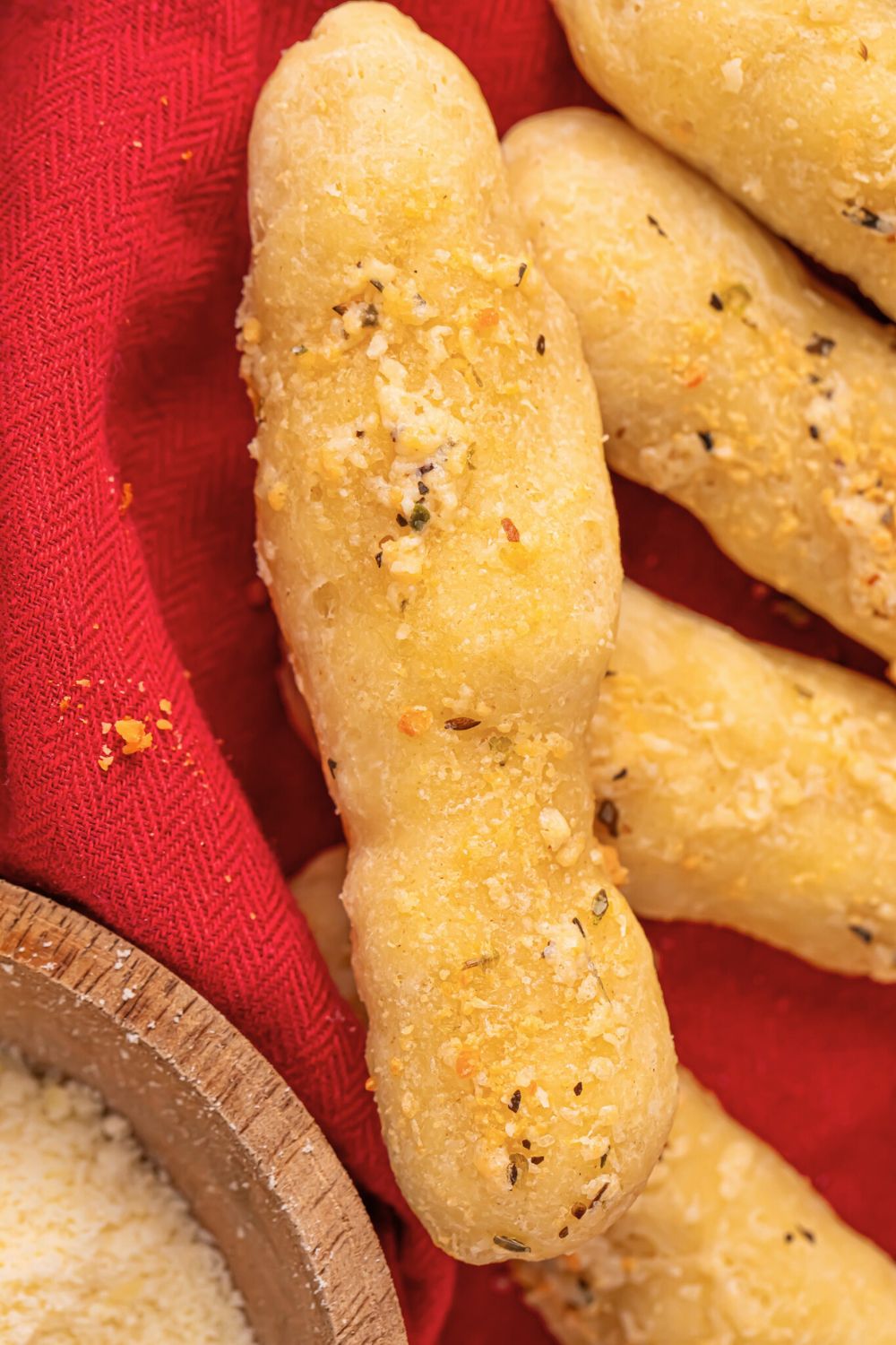 2 ingredient breadsticks in a basket with a red towel and some parmesan cheese to the side 