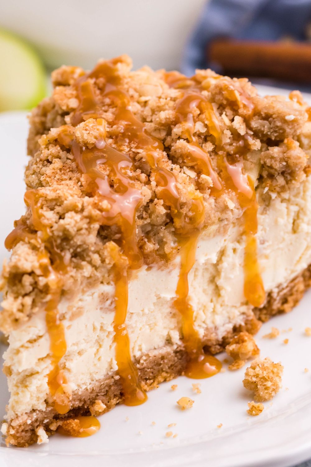 close up slice of Caramel Apple Crisp Cheesecake on a plate with caramel dripping down 