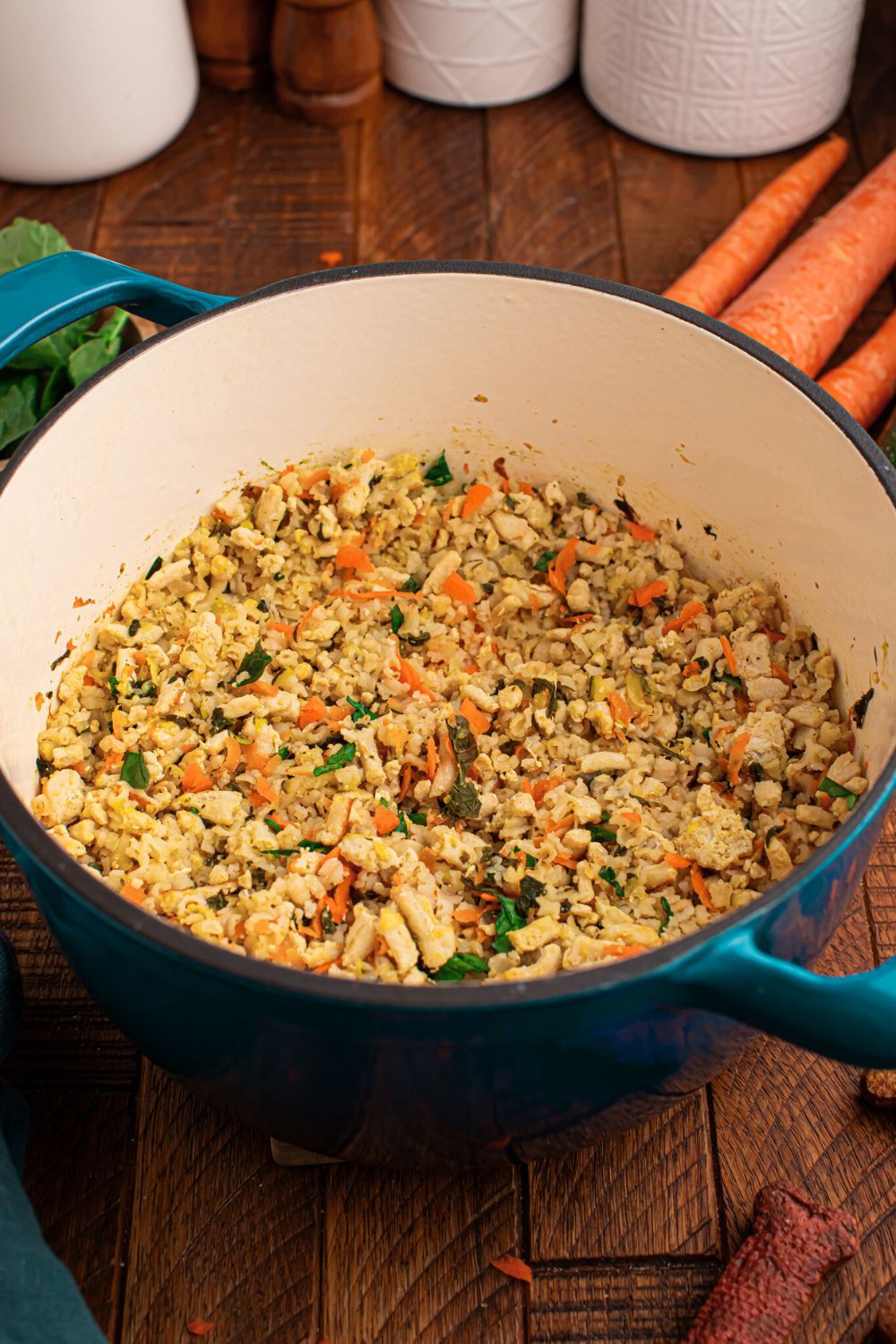 Cooked dog food in a pot sitting on table with carrots and other ingredients around table 
