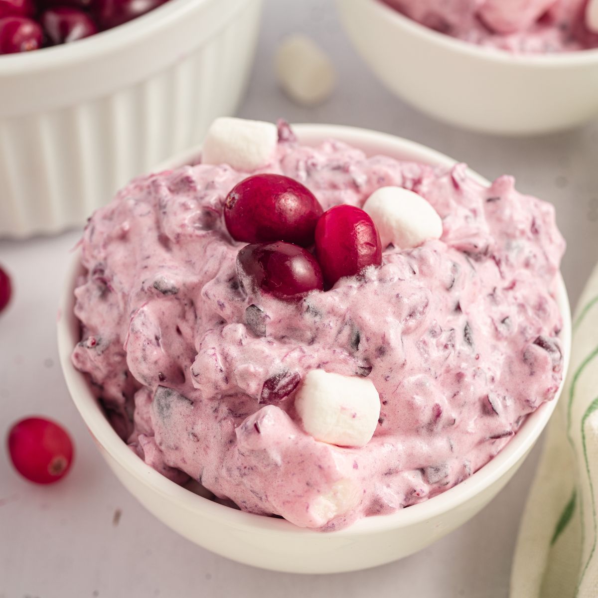 counter with a white bowl with Cranberry Fluff Salad in it topped with fresh cranberries and mini marshmallows 
