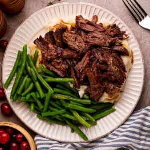 Cranberry Pot Roast on plate with mashed potatoes and fresh green beans and a fork to side on table