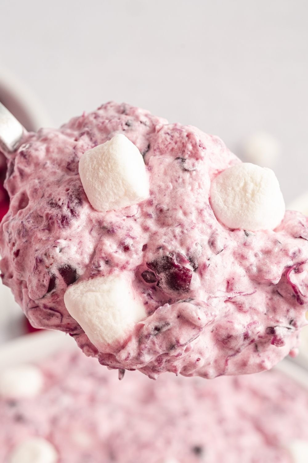 a spoon full of Cranberry Fluff Salad being held above a bowl of the fluff salad on a white table 