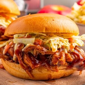 Crockpot Apple Butter BBQ Pulled Chicken sandwich on table with coleslaw on top of sandwich