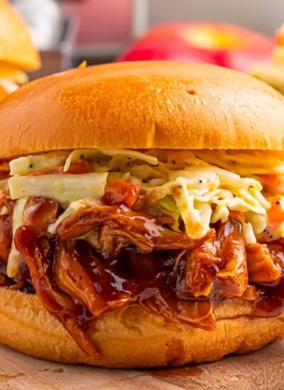 Crockpot Apple Butter BBQ Pulled Chicken sandwich on table with coleslaw on top of sandwich