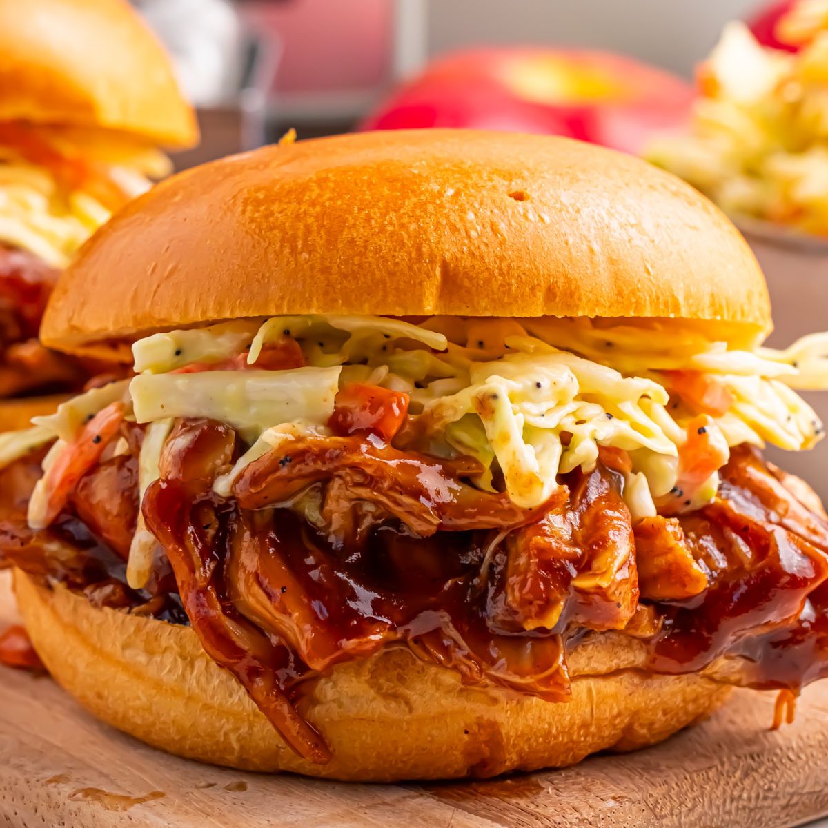 Crockpot Apple Butter BBQ Pulled Chicken sandwich on table with coleslaw on top of sandwich
