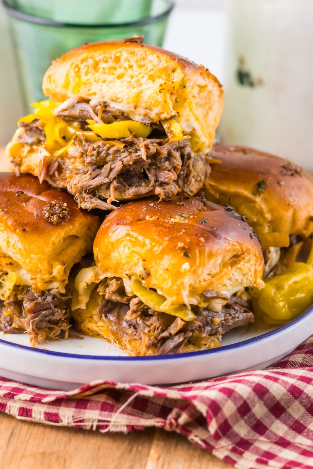 Slow Cooker Mississippi Pot Roast Sliders stacked on plate with a red checkered towel under the plate 