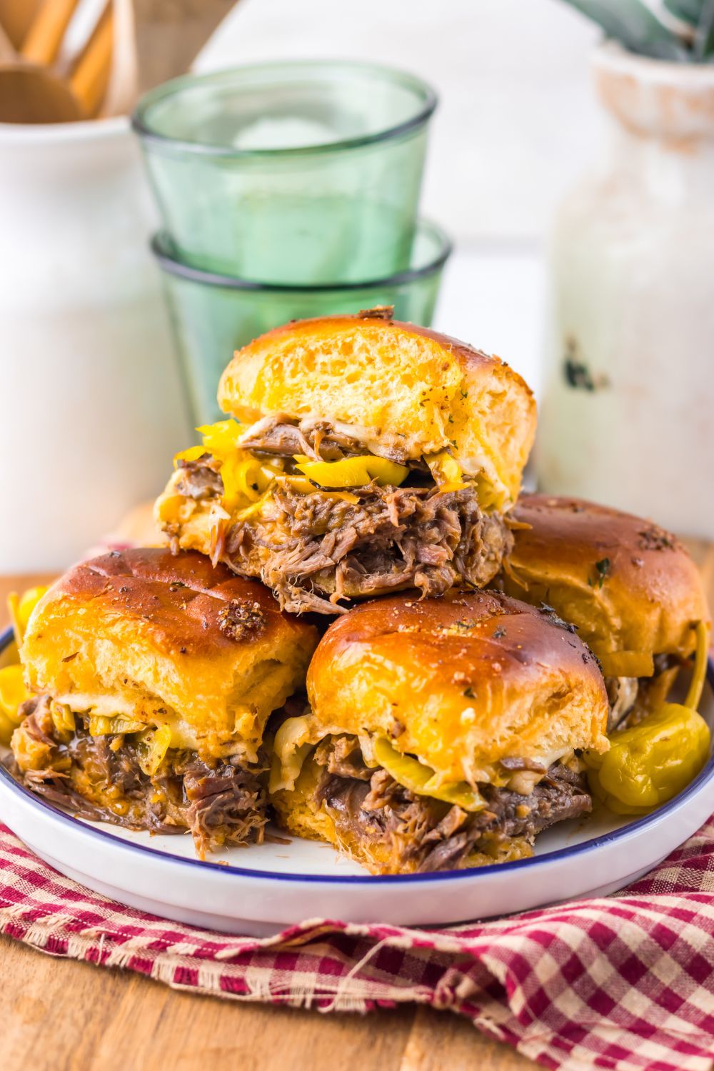  Mississippi Pot Roast Sliders stacked on a plate with glasses behind the plate 