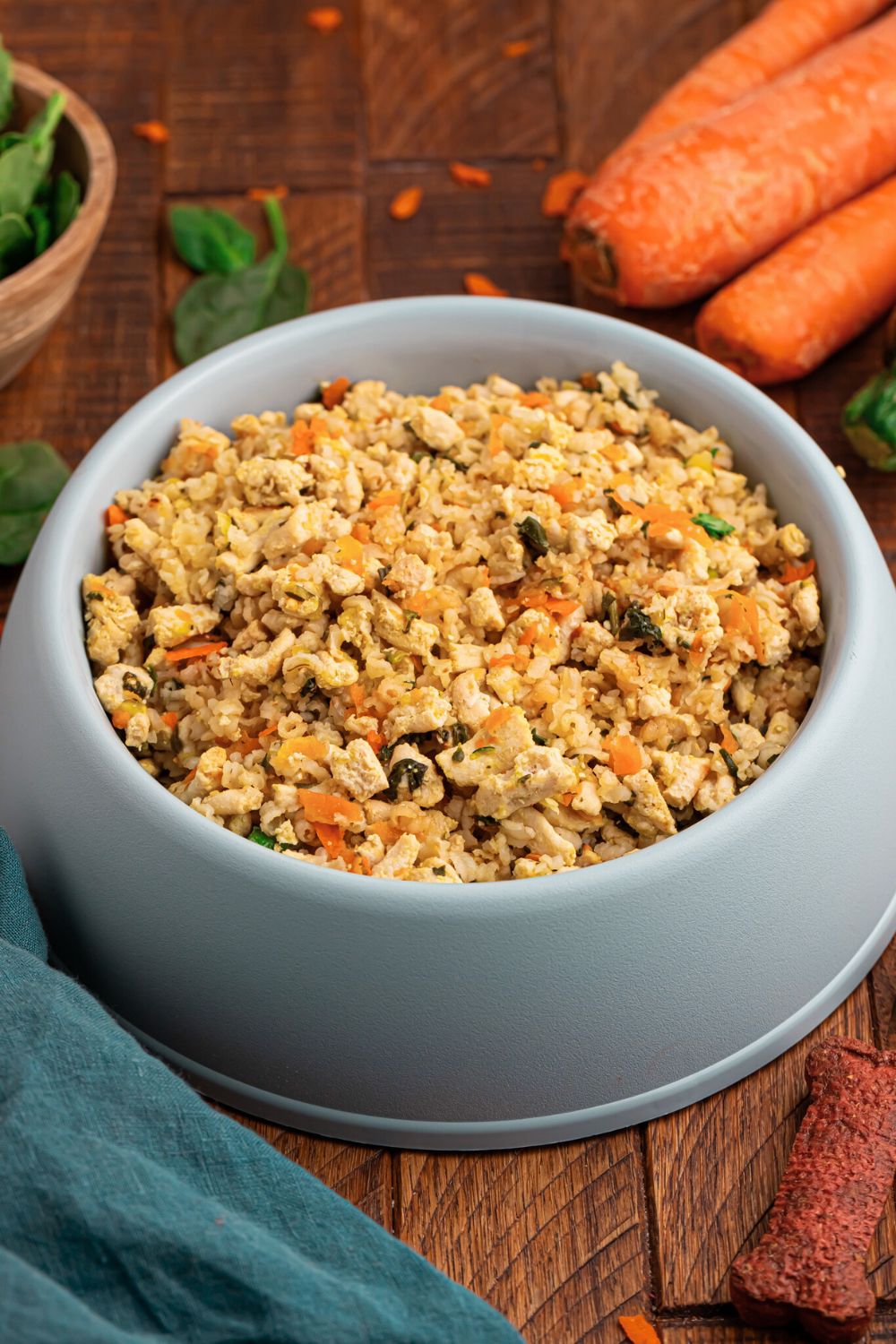 Homemade Turkey and Rice Dog Food with Veggies in a grey bowl on table with herbs and carrots behind bowl 