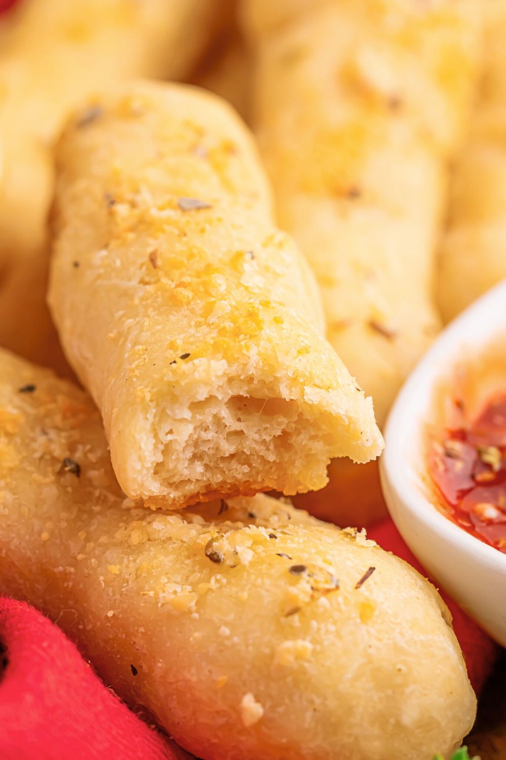 2 ingredient breadsticks on table with one having a bite taken out of it and a bowl of sauce to side of breadsticks 