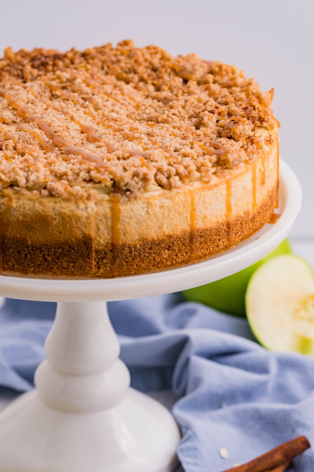 Caramel Apple Crisp Cheesecake on a pie plate with some green apples to the side 
