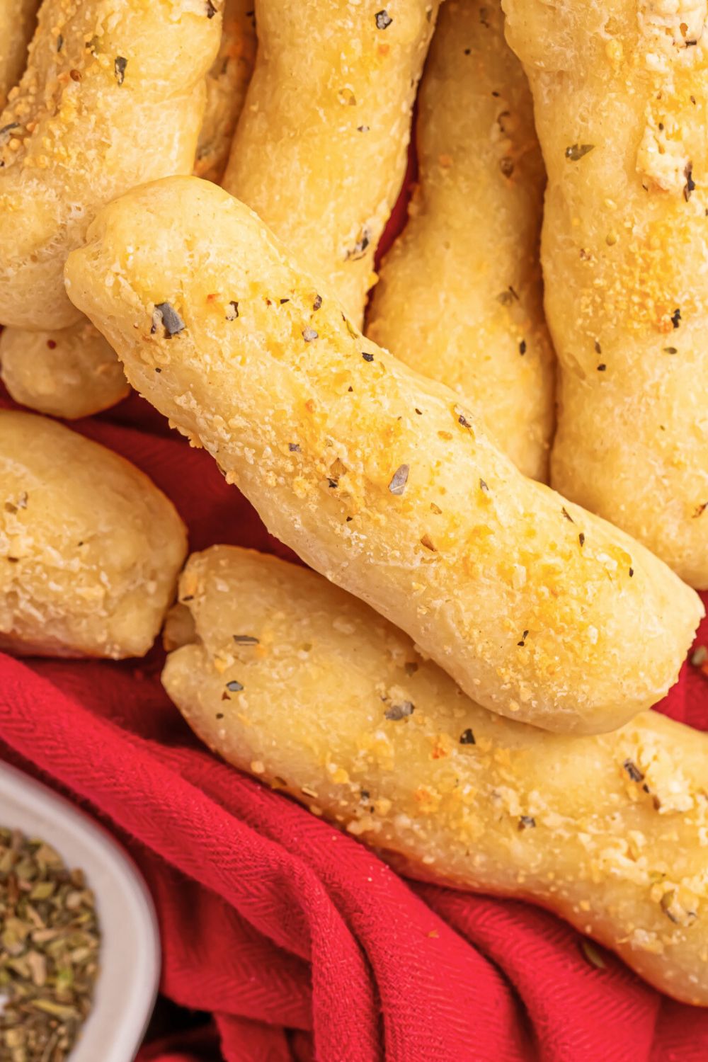 2 Ingredient Garlic Parmesan Breadsticks stacked on a red towel with seasoning in a bowl to side 