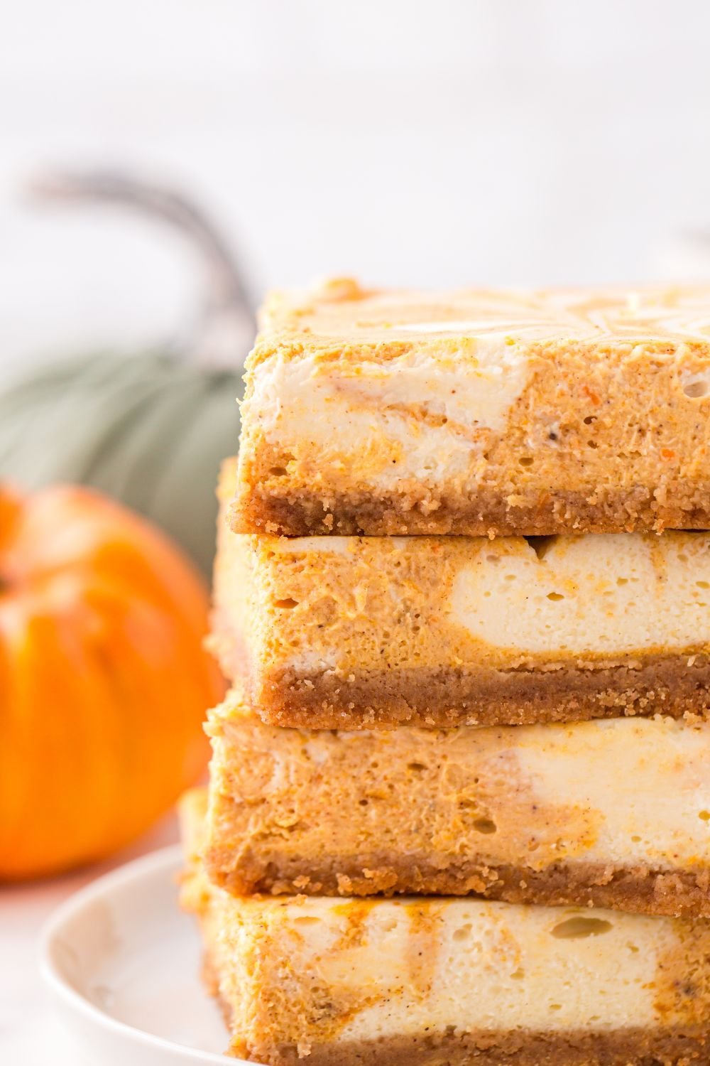 Swirled Pumpkin Cheesecake Bars stacked on table with pumpkin to side