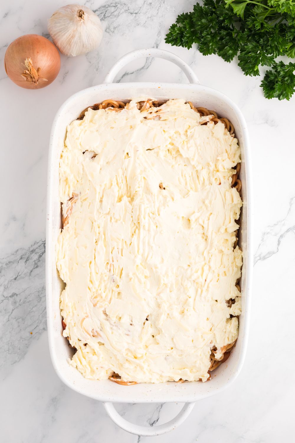 Million Dollar Spaghetti Casserole being assembled in a pan on table 