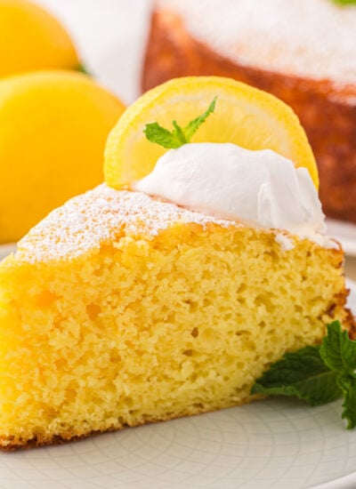 Slice of Italian Lemon Ricotta Cake on a white plate with sliced lemons