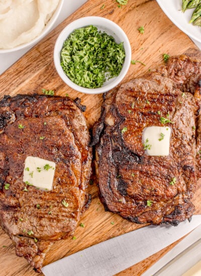 Grilled Ribeye Steak sliced on cutting board topped with pats of butter