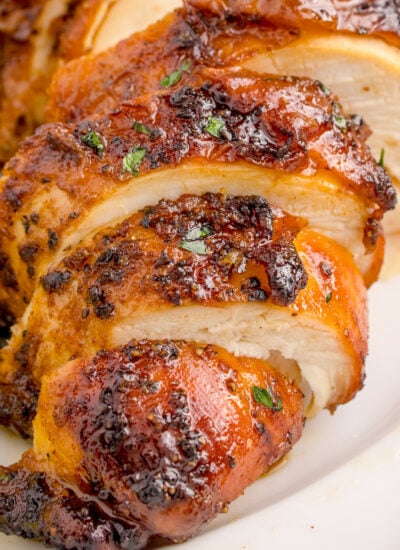 Air Fryer Chicken Breast sliced on table with some vegetables to side of the chicken