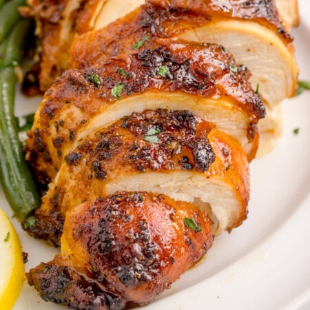 Air Fryer Chicken Breast sliced on table with some vegetables to side of the chicken