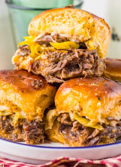 Slow Cooker Mississippi Pot Roast Sliders stacked on a plate sitting on a table