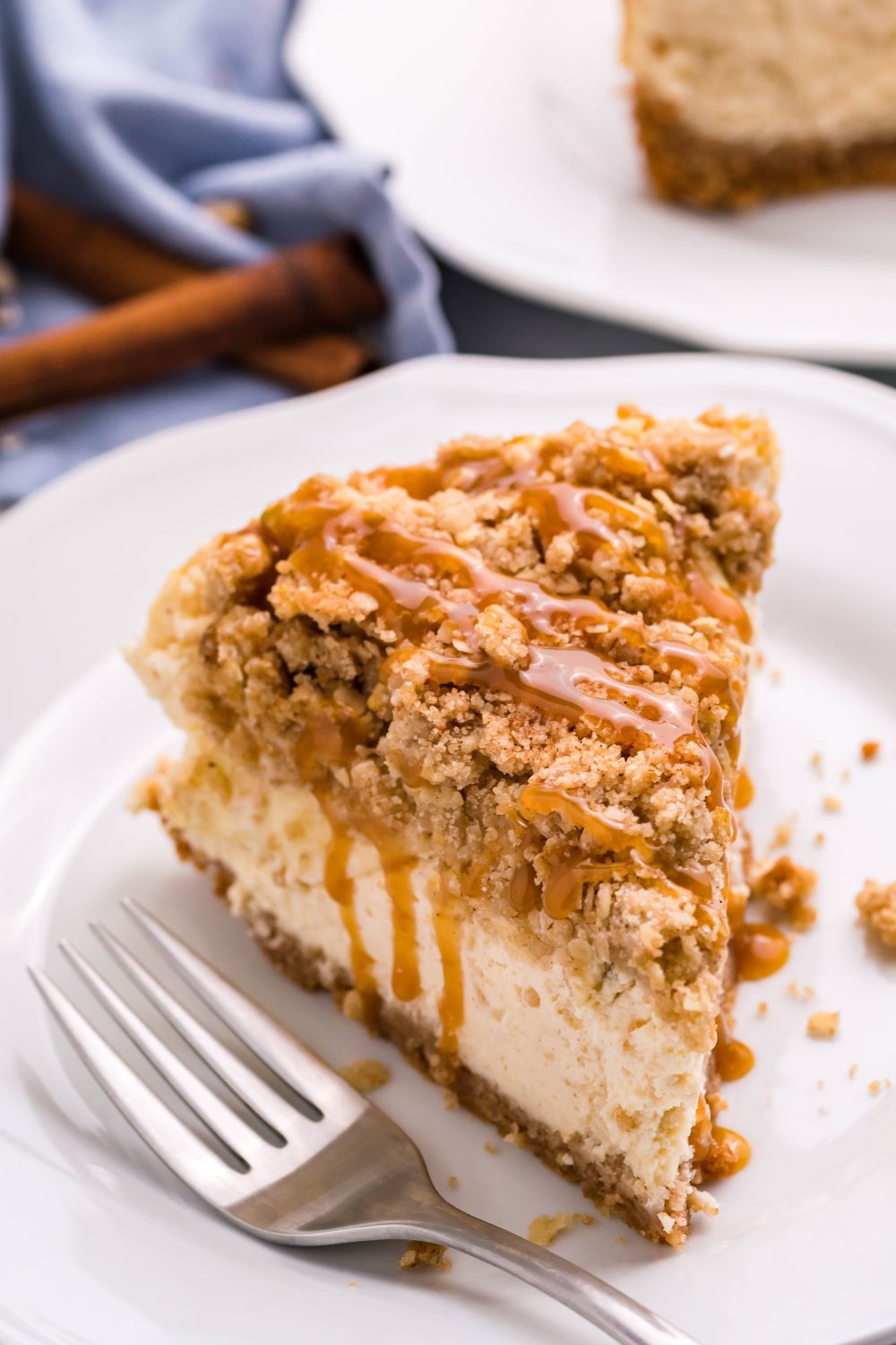 slice of Caramel Apple Crisp Cheesecake on plate with a fork to side of cheesecake