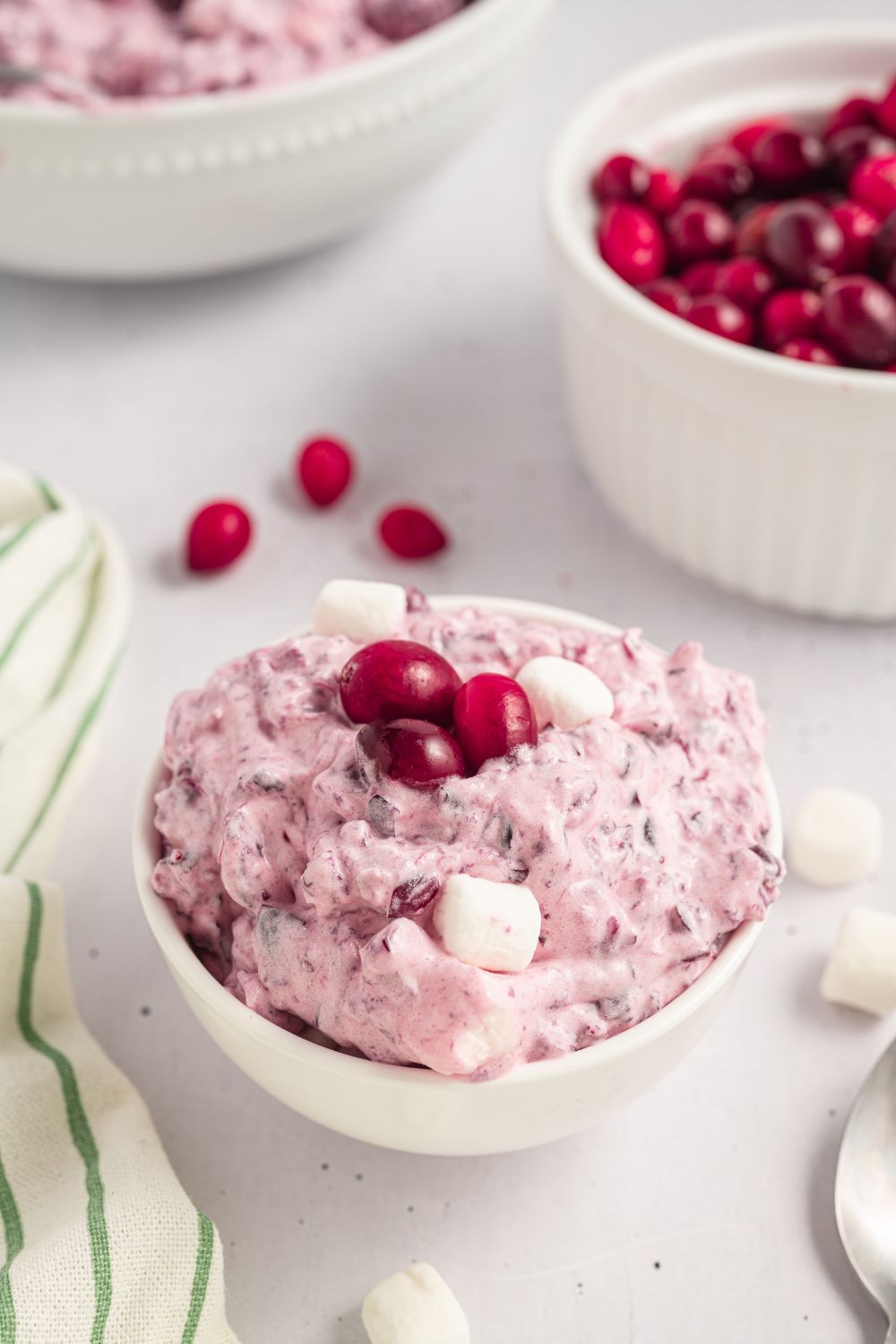 Cranberry Fluff Salad in a white bowls on table with a bowl of cranberries in another bowl, and a striped towel to side of table 
