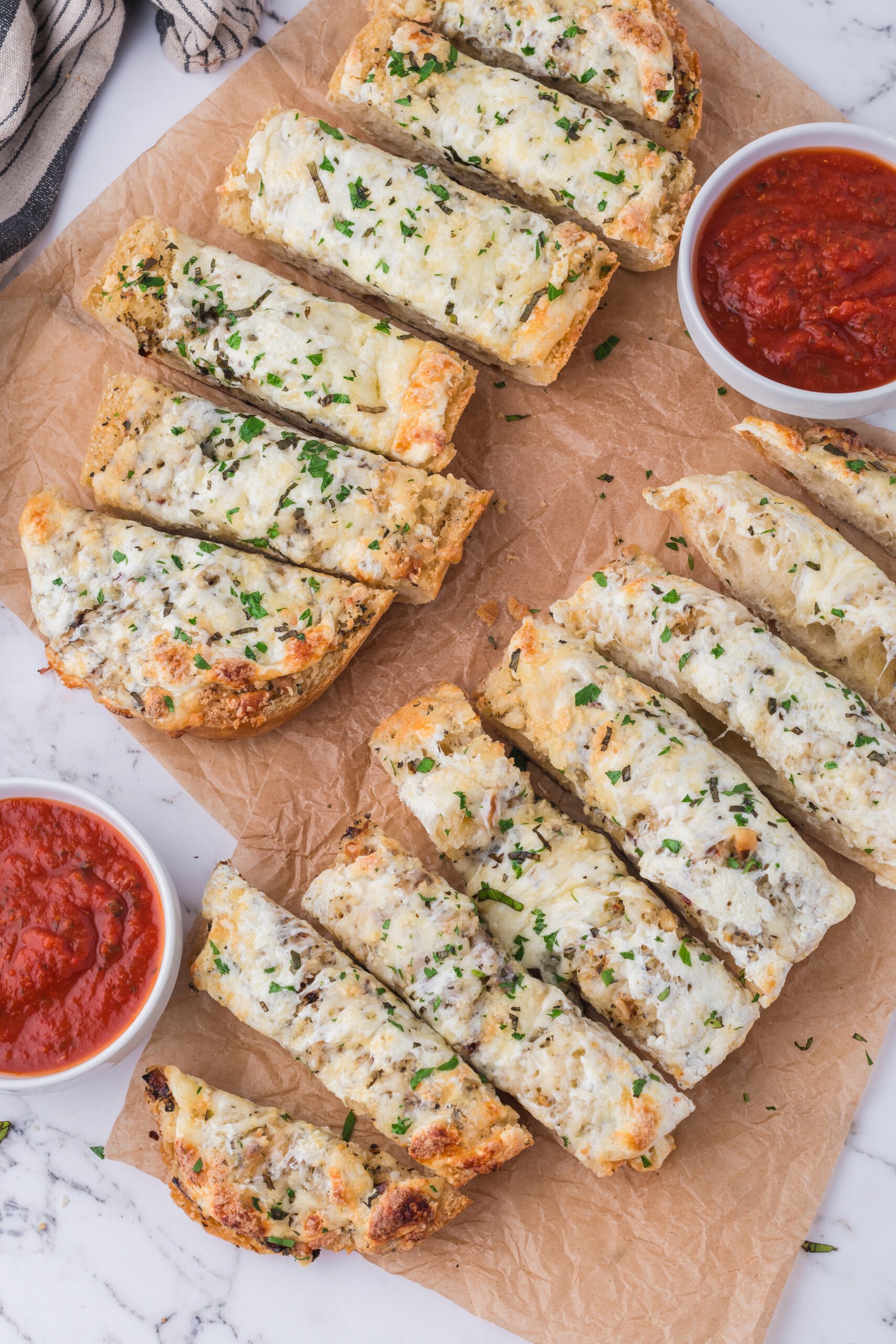 overhead look at table with cutting board with sliced Cheesy Garlic Bread on it and marinara sauce in bowls 