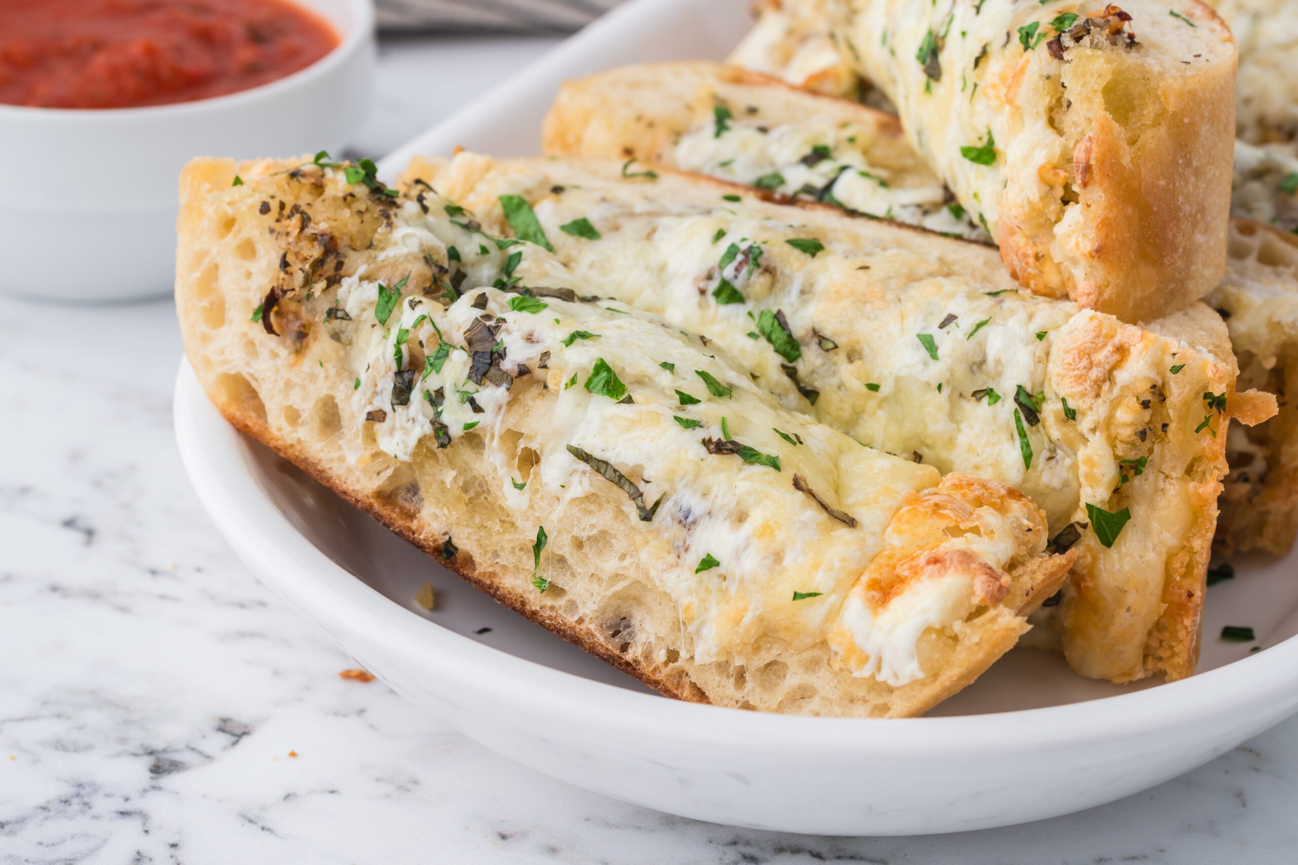 Cheesy Garlic Bread sliced in a white plate with a bowl of marinara next to it