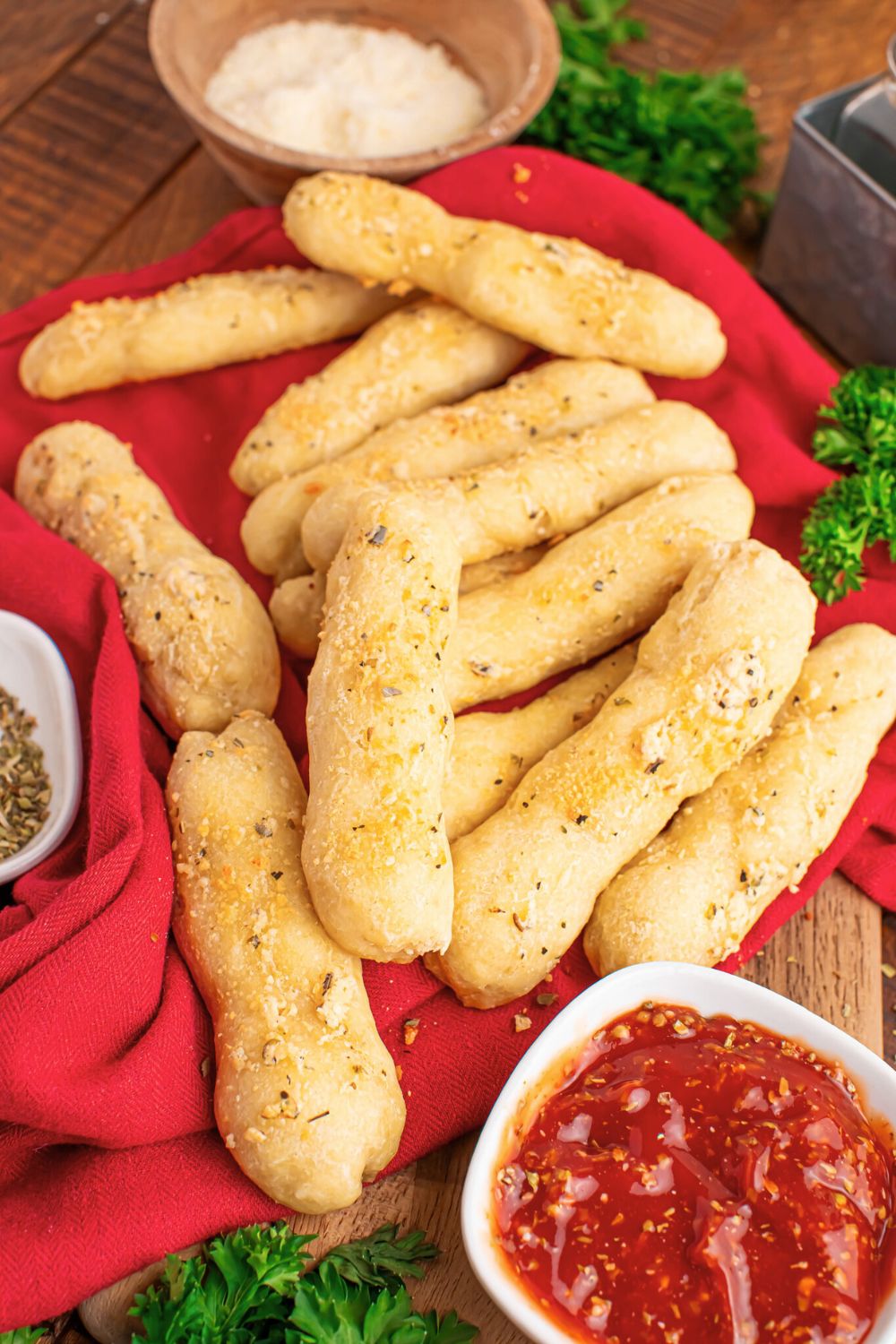 red towel on table with 2 Ingredient Garlic Parmesan Breadsticks scattered on table with some dipping sauce in a bowl to the side 