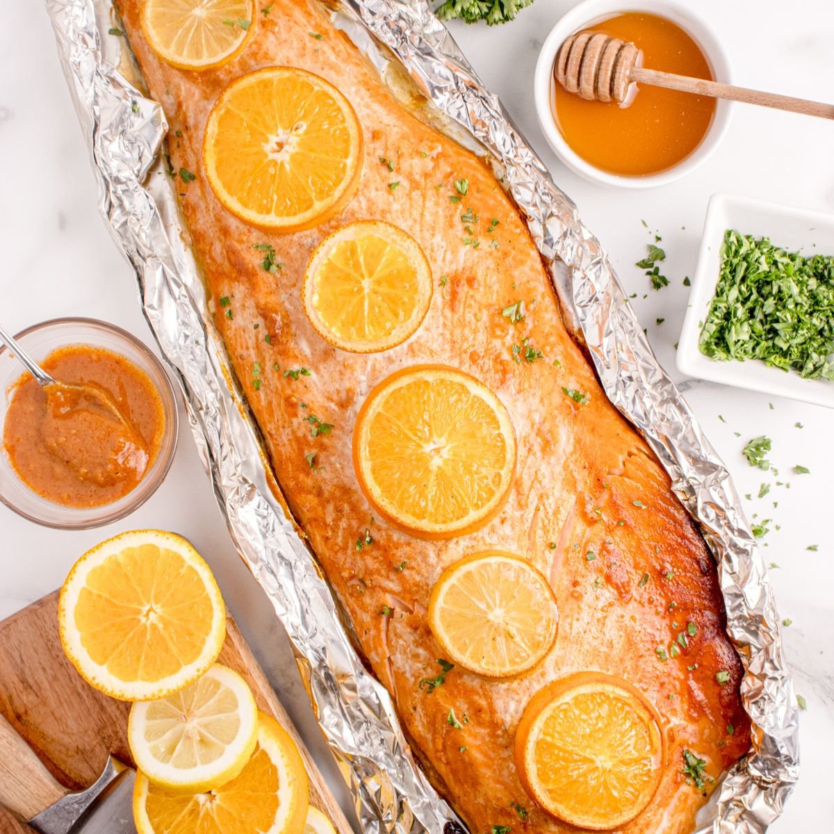 Grilled Honey Mustard Salmon in Foil on table with honey, citrus wedges, etc. 