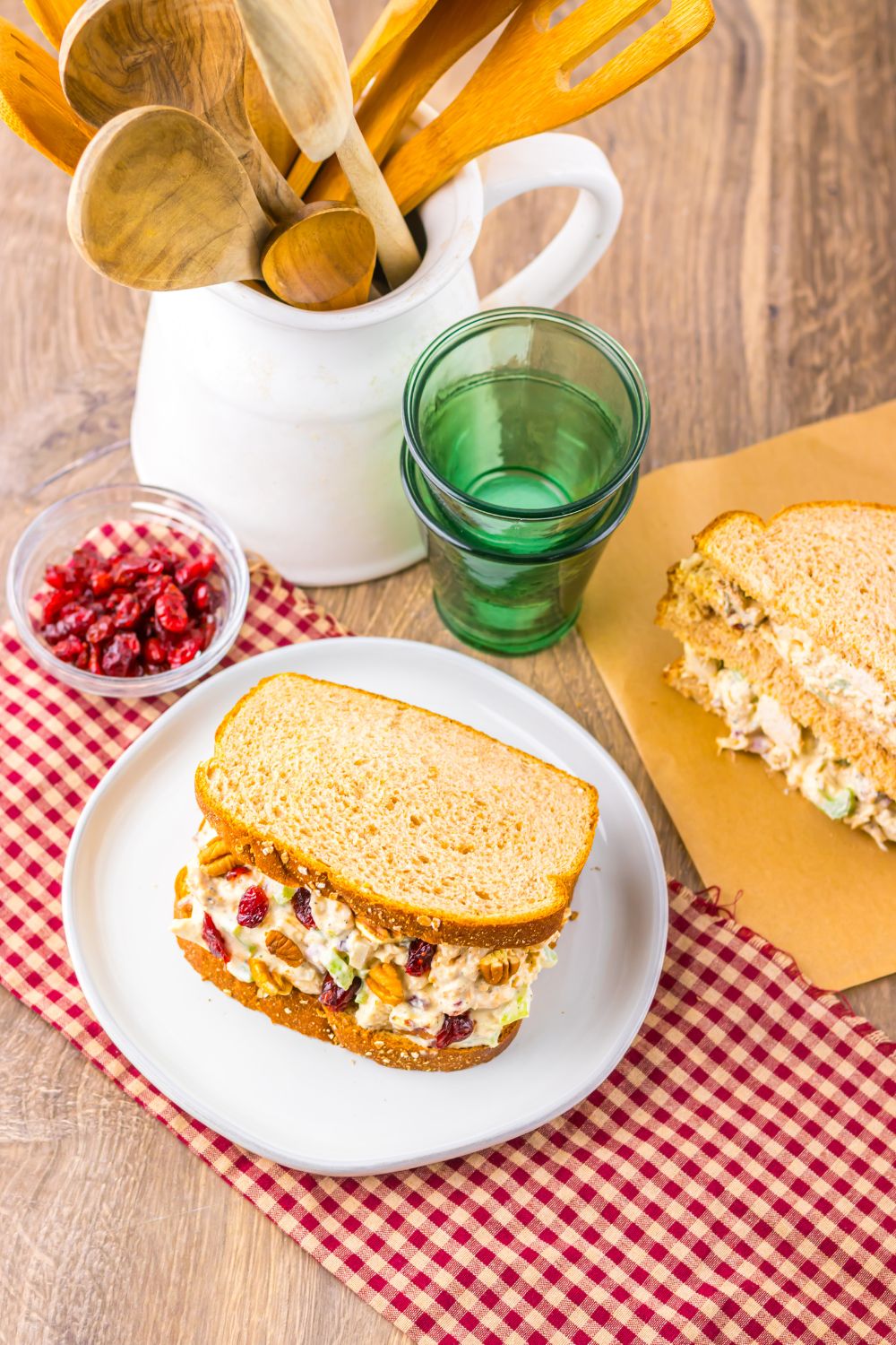 Thanksgiving Turkey Salad on plates with another sandwich on a cutting board, and a bowl of cranberries to side 
