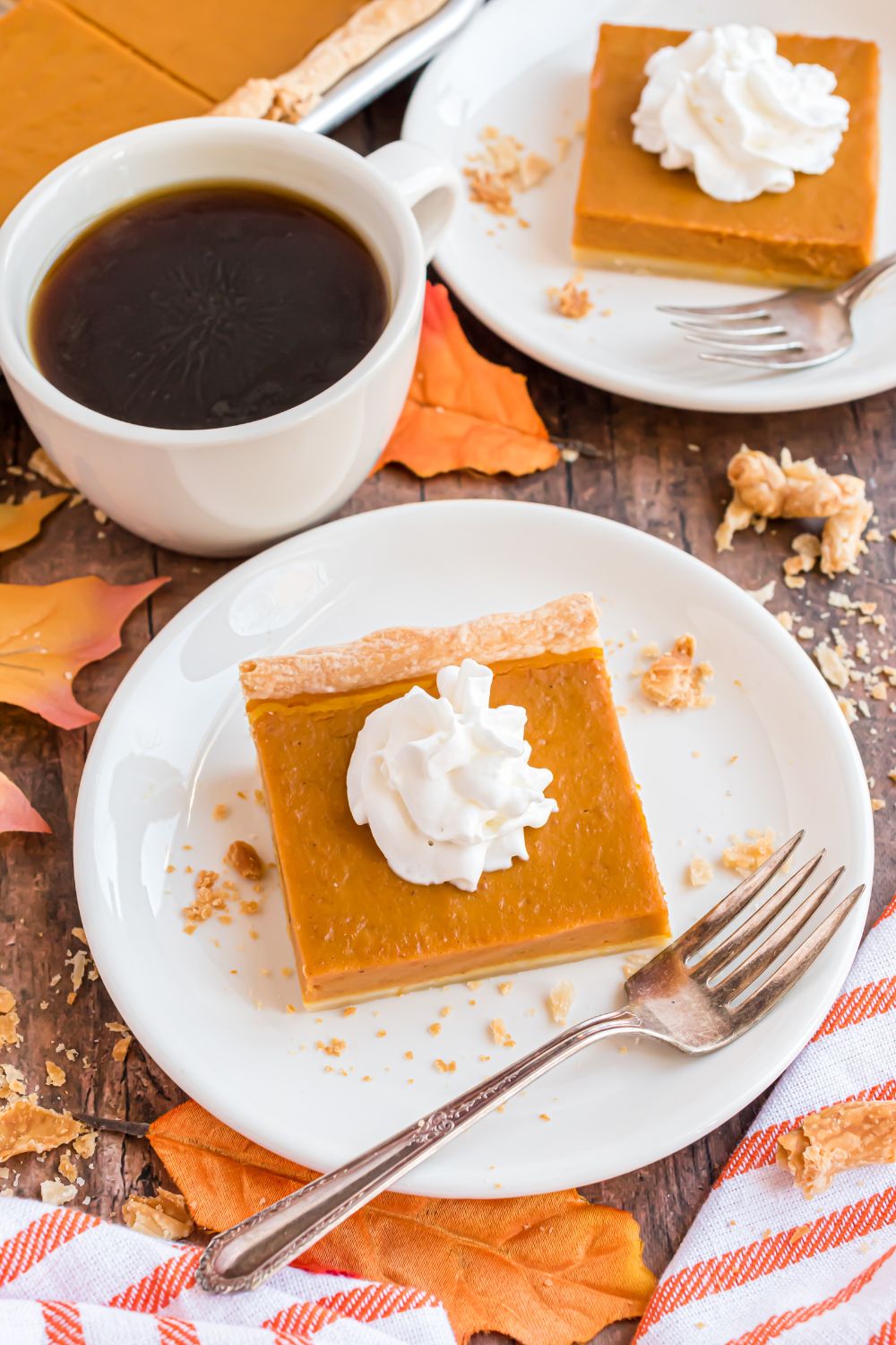 wooden table decorated like fall with plates of square Sheet Pan Pumpkin Pie slices on each plate and a cup of coffee in between the plates 