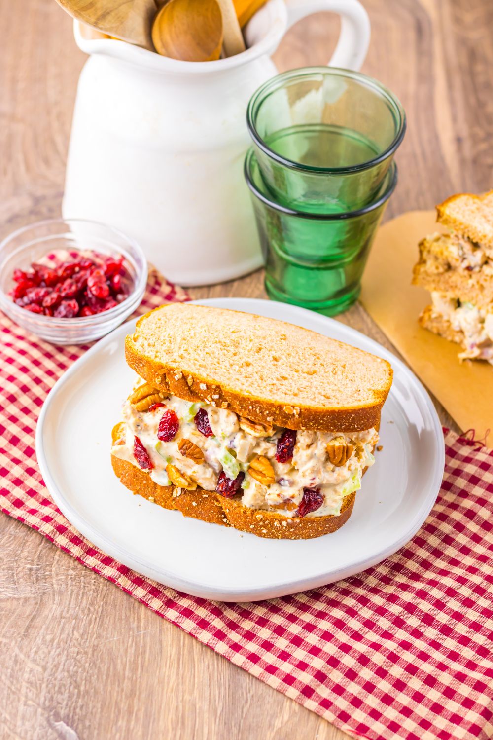 Thanksgiving Turkey Salad sandwiches pn plates with glasses, and a bowl of cranberries to side by a napkin
