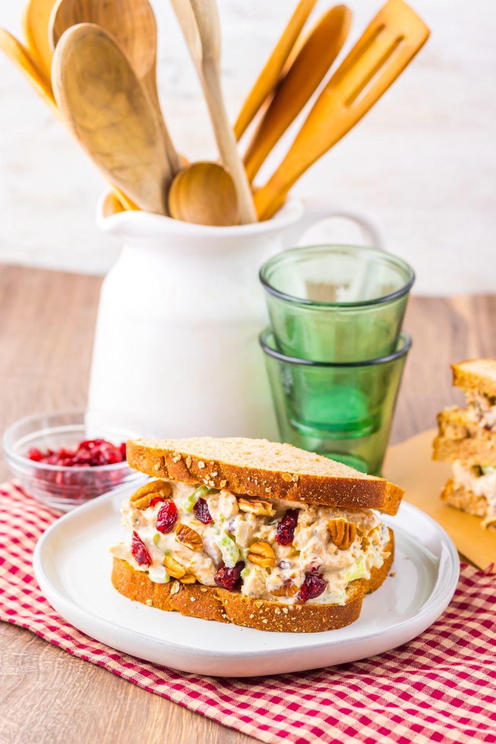 Thanksgiving Turkey Salad sandwich on table with glasses to side, and a container with spatulas and such inside 