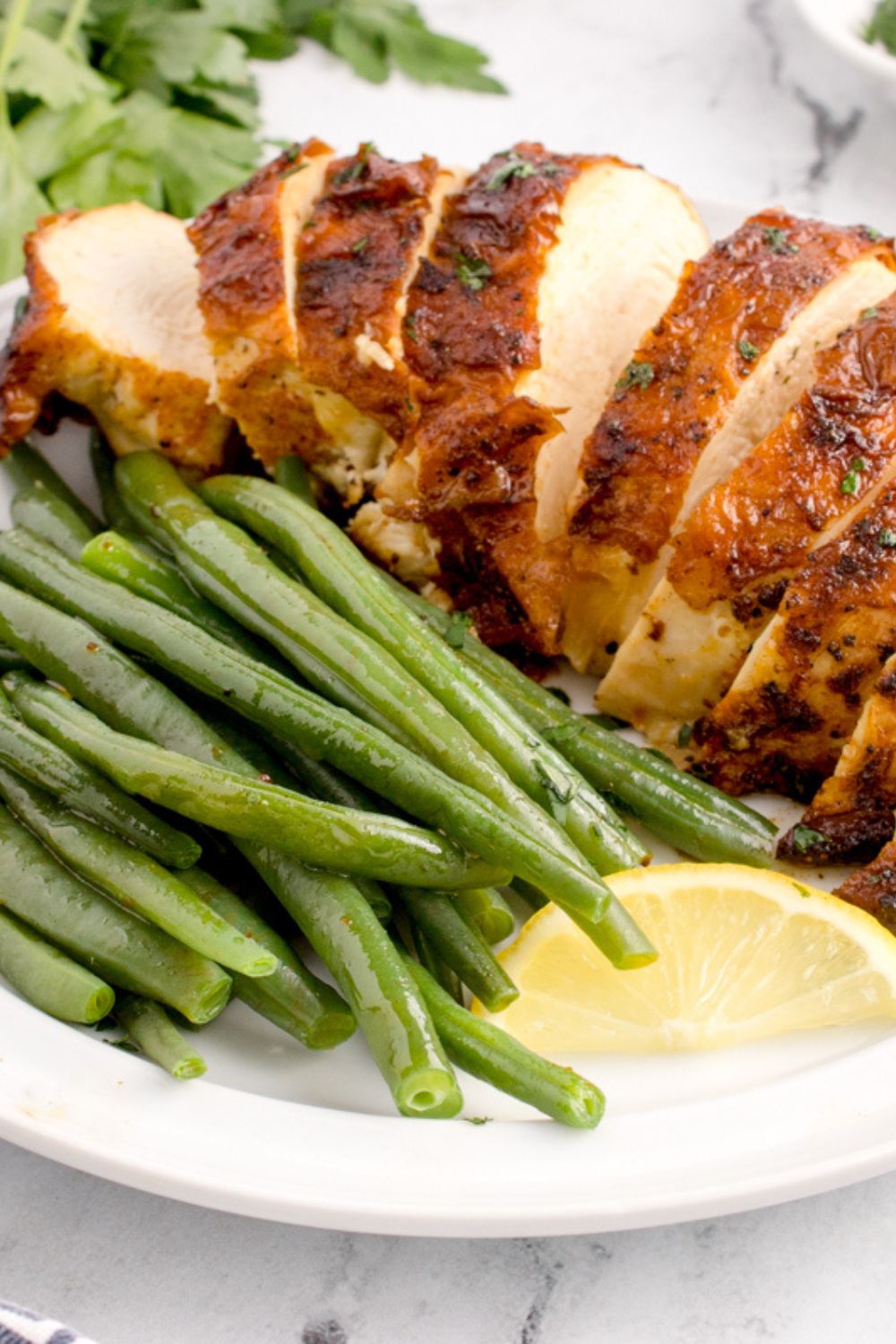 Air Fryer Chicken Breast sliced into strips with green beans and a lemon wedge 
