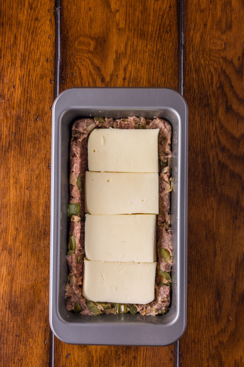 half of meat topped with provolone cheese in a loaf pan to make Stuffed Philly Cheesesteak Meatloaf