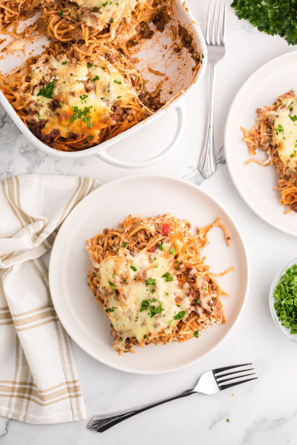 Million Dollar Spaghetti Casserole in pan and then some in plates on table 
