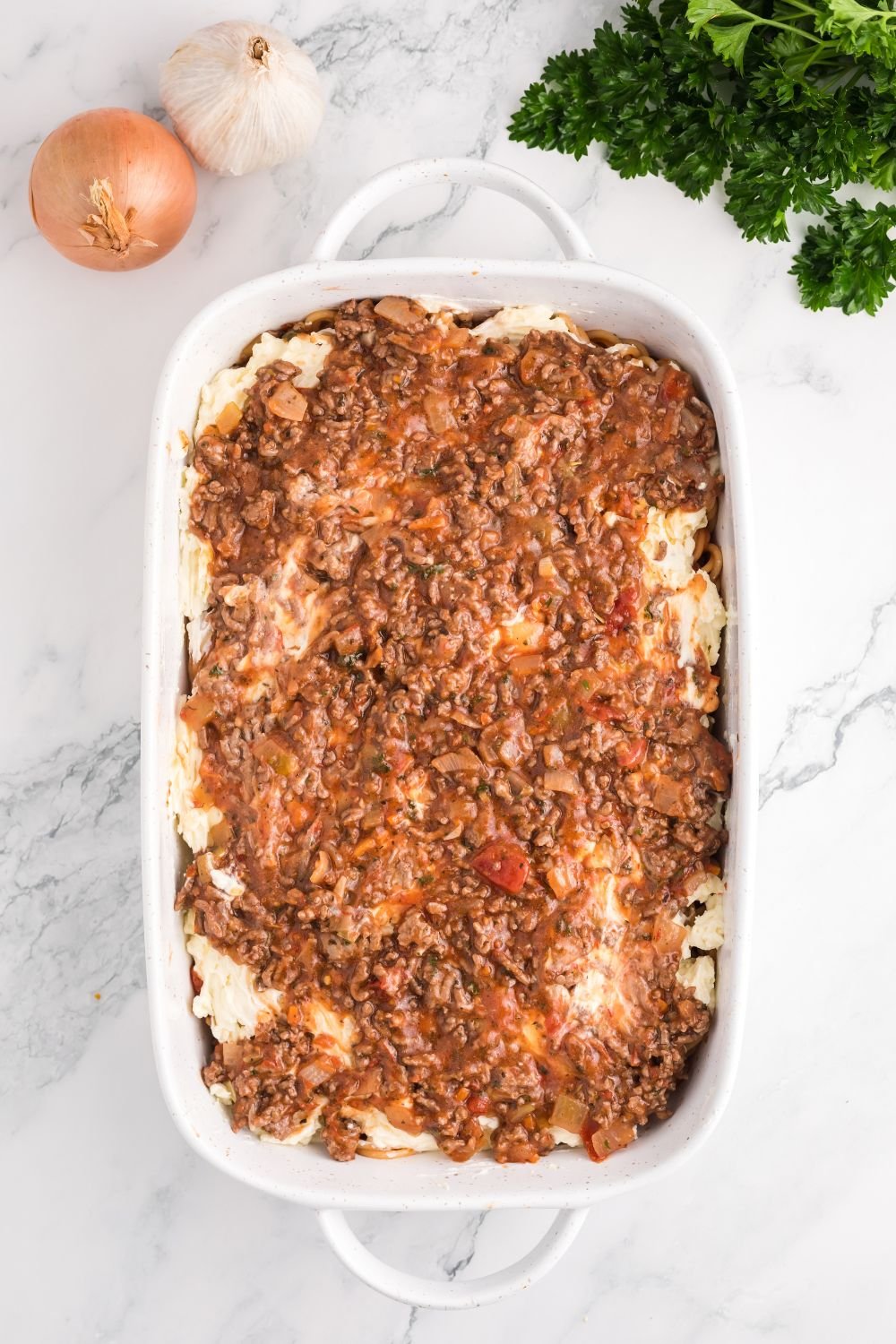 Million Dollar Spaghetti Casserole being assembled in a pan on table 