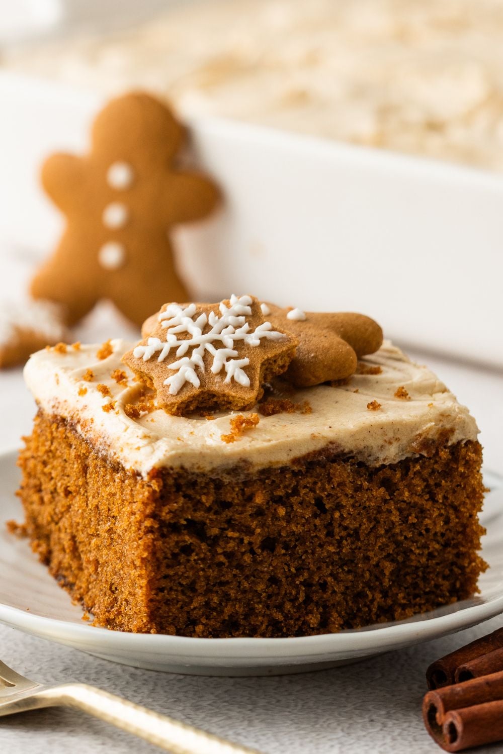 slice of Gingerbread Cake with Cream Cheese Frosting on plate with a gingerbread cookie behind plate