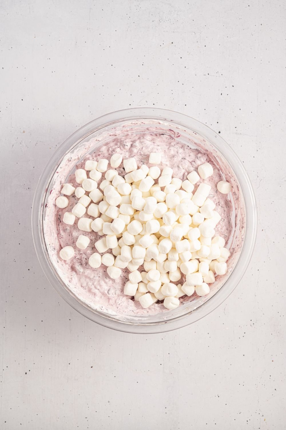 marshmallows on top of cranberry salad being assembled in the glass bowl 