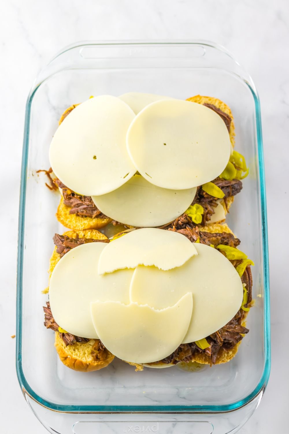 provolone cheese on top of meat and peppers in a casserole pan